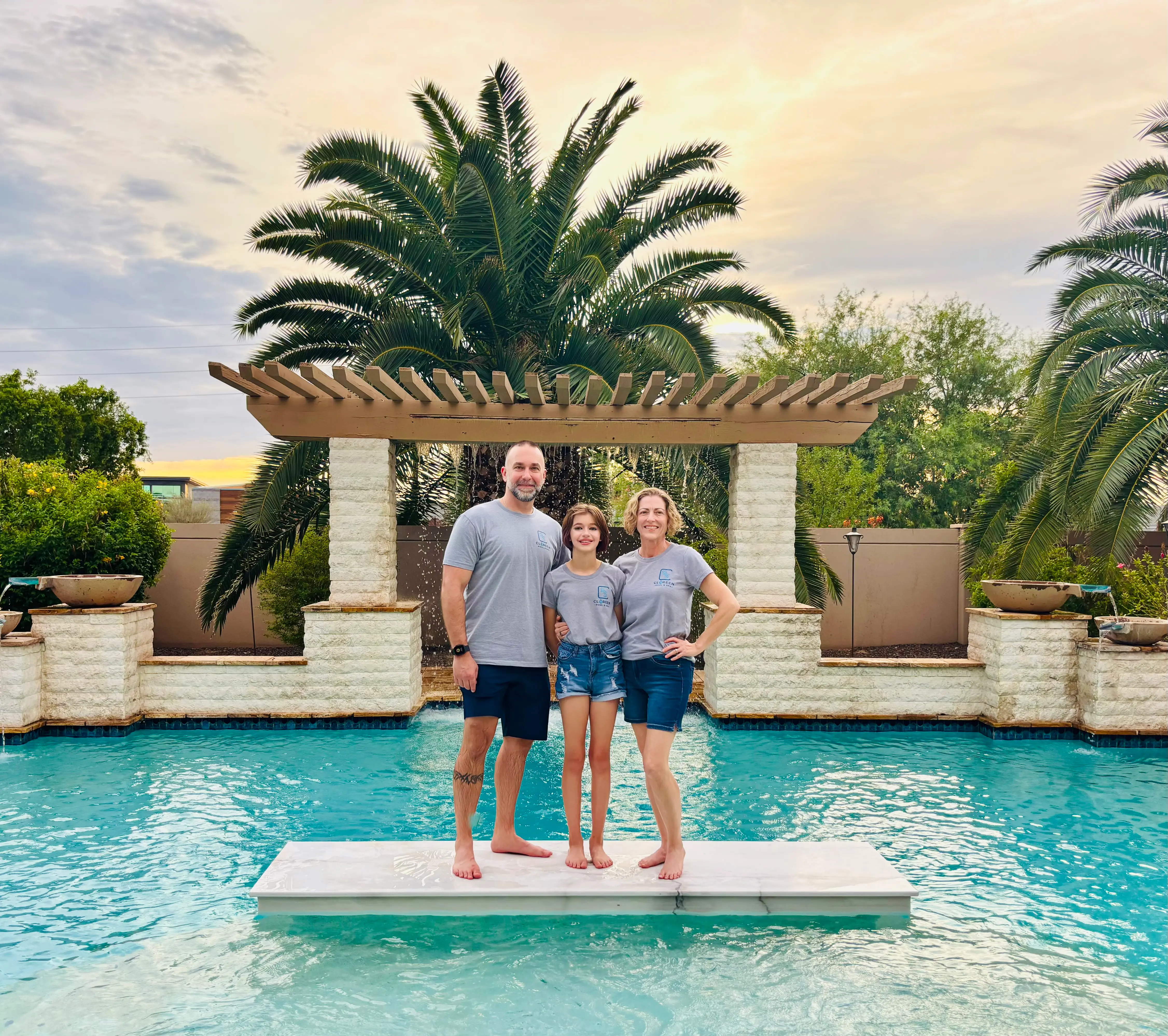 Scott, Sage, and Tina Clore standing together by their backyard pool waterfall